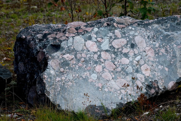 Ein grosser grauer Felsen mit vielen runden Einschlüssen von rosa Granit.