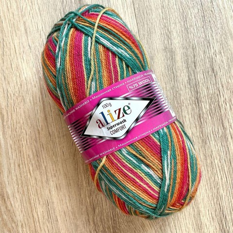 A ball of self-patterning sock yarn in pink, yellow, orange, and petrol colors on a light wooden background.