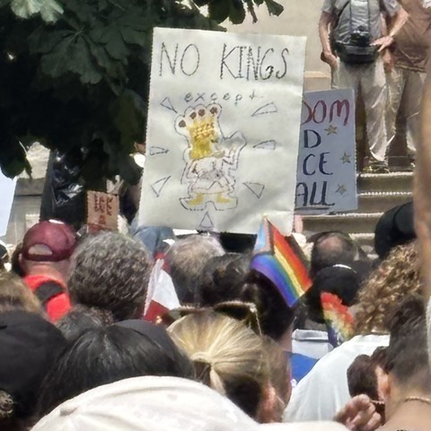 A protest sign above a crowd of people that reads, “No Kings except Pizza King!”