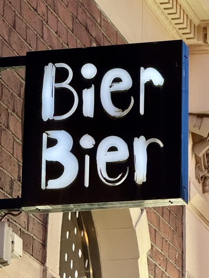 A sign reading "Bier Bier" in bold, illuminated letters, mounted on a brick wall.