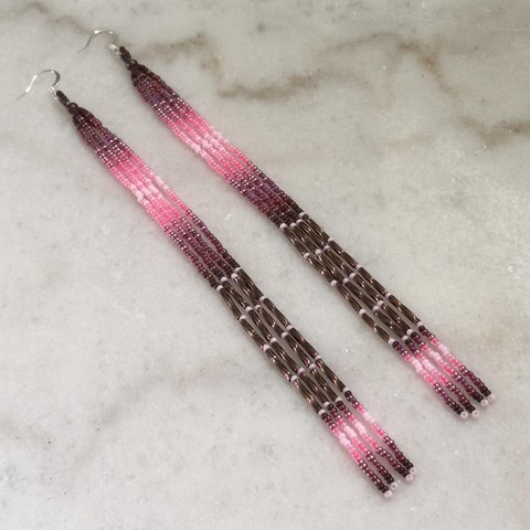 A pair of long beaded dangle earrings in shades of pink and brown against a white marble background