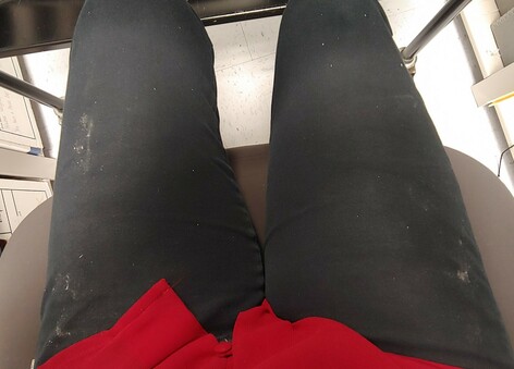 Legs of a person sitting in a chair. They are wearing black pants and a red shirt. The pants are covered in dust. 