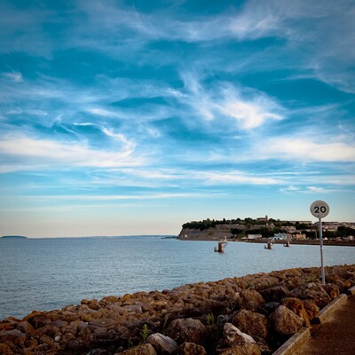 A photograph of Penarth headland taken from the Barrage in Cardiff, South Wales. The tide is high and the sky is full of wispy clouds.