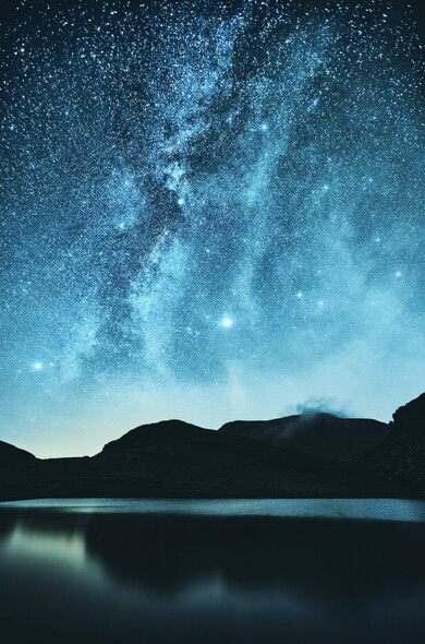 The stars and the Milky Way are seen above a mountain lake in Eryri. The night sky filled with stars.