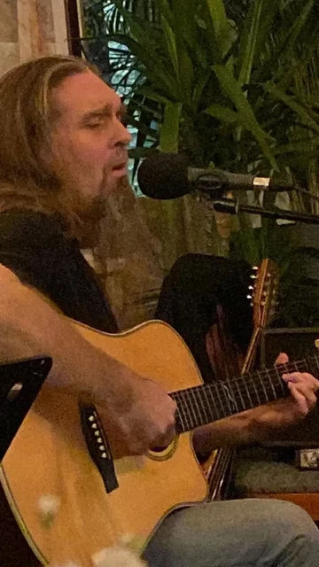 Acoustic guitar with long hair and long beard player singing into microphone 