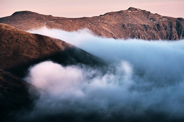 Yr Wyddfa in Eryri catches the last of the day's light as soft clouds roll in across the lower slopes. 

The mountain captures the warm colours of a winter sunset. The clouds look cooler in tone, possibly bringing snow.