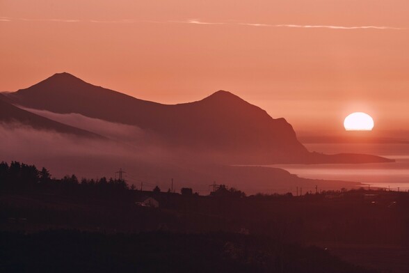 The sun sets into the sea as the hills of Yr Eifl roll down to the coast. A low, misty cloud starts to creep in over the landscape. 