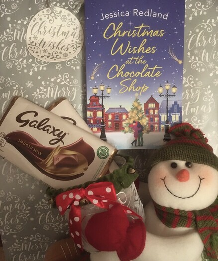 Book cover of Jessica Redland’s Christmas book, a smiling snowman decorationholding a container of Chocolate 