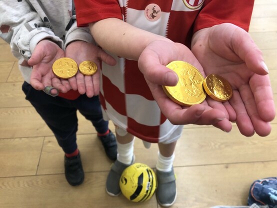 Picture of two children holding out the gold chocolate coins they received (two each) in football school today. There is a yellow football at the feet of the older one. 