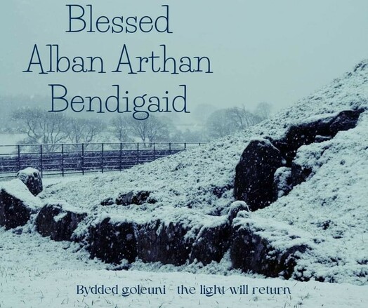 A photo of a snow covered Bryn Celli Ddu burial chamber with the text "Blessed Alban Arthan Bendigaid" and "Bydded goleuni - The light will return".