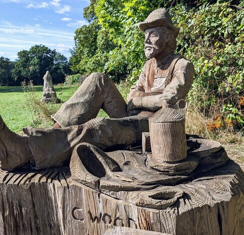 Wooden sculpture of an old man in a hat sat down relaxing.