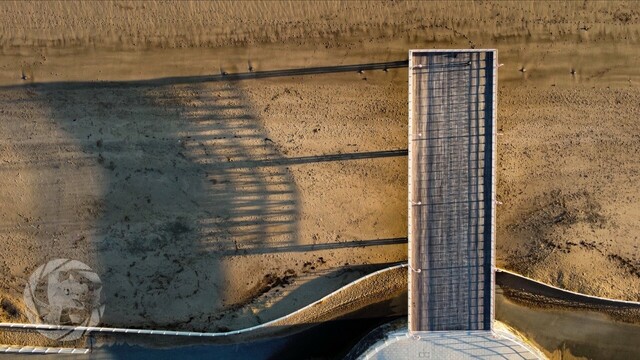 Colwyn bay pier from above with a drone. Pier points up from the promenade path at the bottom of the image. Sunrise, the shadow of the pier and the ironwork underneath is cast to the left.