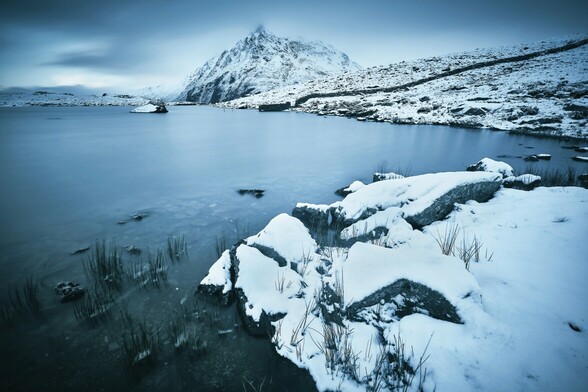 A snow-bound landscape at Cwm Idwal in Eryri. It is dusk. A long exposure brings out the last of the day's light. The mountain Pen Yr Ole Wen is in the background.