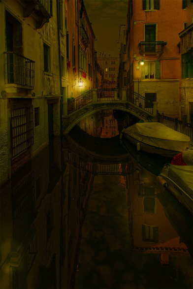 A photo of a dimly lit back street canal in Venice with a footbridge over.