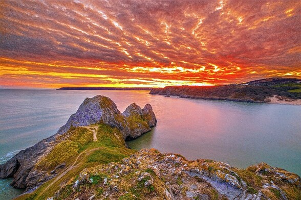 Beautiful mackrell scale sunset sky with deep reds and oranges over Three Cliffs Bay in the Gower, South Wales, United Kingdom