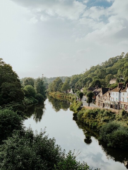Houses nestled near trees and a river. The river is calm and glasslike and gives off a peaceful vibe.