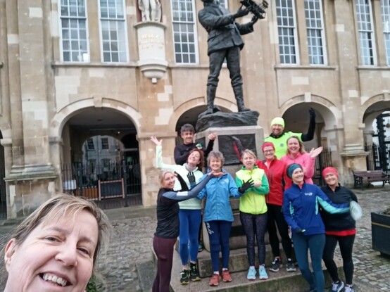 A group of runners in bright clothing standing under the statue of Charles Rolls, the aviator in Monmouth. 
