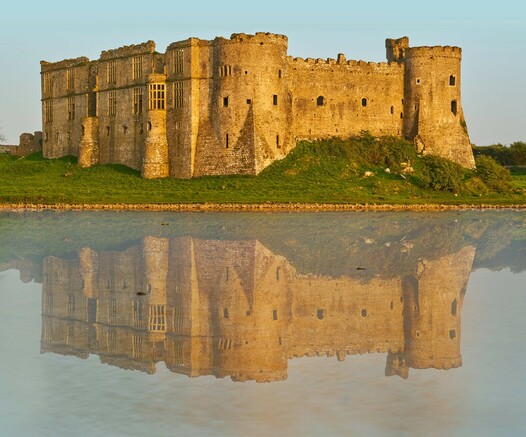 Carew Castle,  a beautiful ancient castle in Pembrokeshire, UK, bathing in golden sunlight with it's reflection in the mill pond.