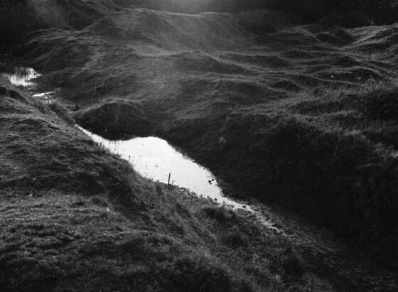Black and white image of a dark landscape with a bright body of water.