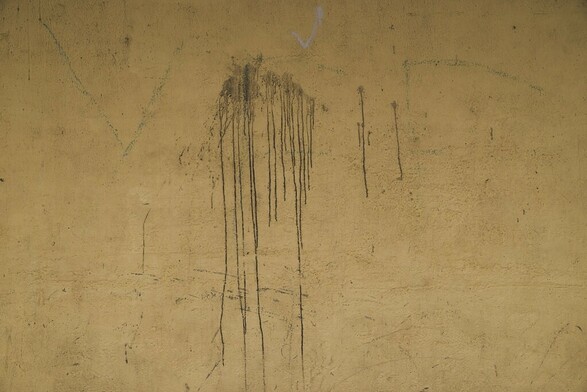 A dirty yellow wall, full of texture and grim with a black liquid running down the wall.