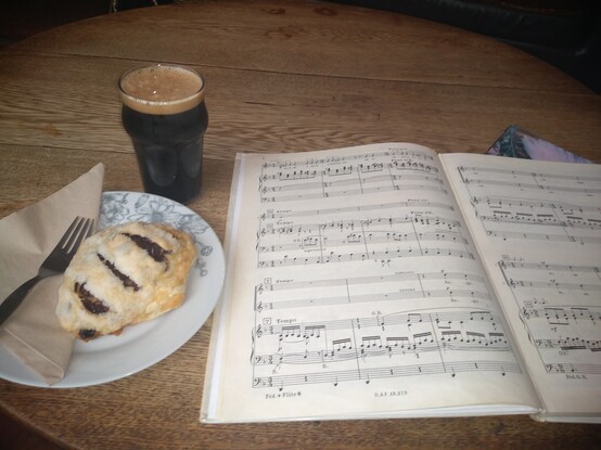 Open copy of music with a delicious looking Eccles cake and a half pint of a dark and creamy stout 