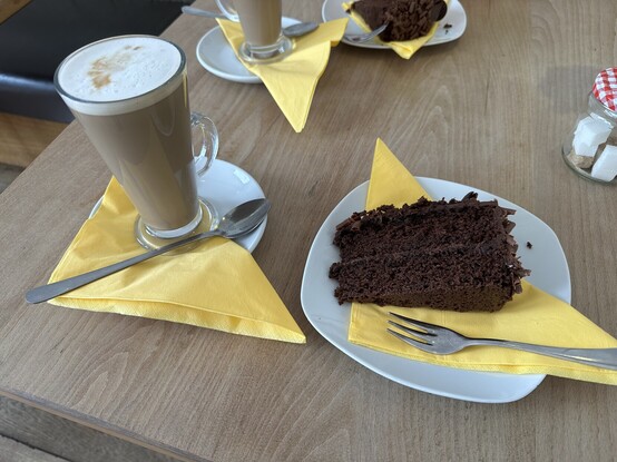 A latte in a glass mug and a slice of chocolate cake on a white plate. 