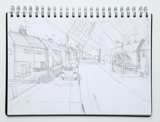 Photo of sketchbook with pencil drawing of a residential street.