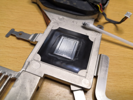 Underside of a laptop heatsink (the part in contact with the CPU die) after cleaning the entire underside. The blackened cotton swab used to clean it is resting on it.