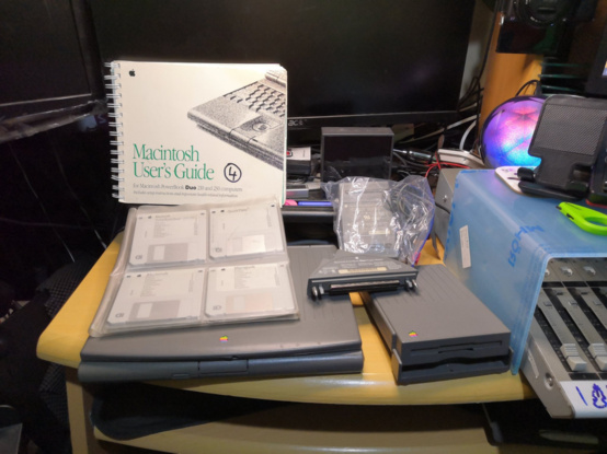 Mac Powerbook Duo 230 laptop with floppy disk drive and adapter, restore floppy disks, and Macintosh User's Guide.