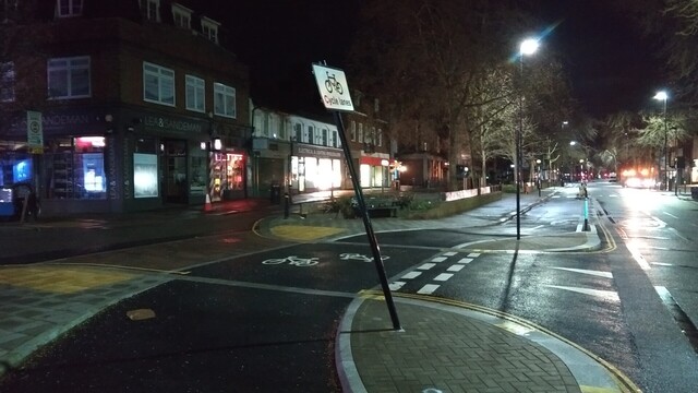 A cycle lane at night, with a 'cycle lane' sign that has been bent back from vertical