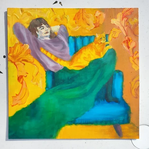 A square painting of me curled up and lounging back off to the side on a comfy blue chair. I am wearing a pink jumper and a flowing green skirt. My ginger cat Rusty is on my lap looking majestic. The background is orange and there's a nice leaf pattern that functions a bit like a border. It's an oil painting, overall quite vivid and I was inspired by pre-raphaelite paintings and William Morris, but someone else has made a connection with 1920s French art