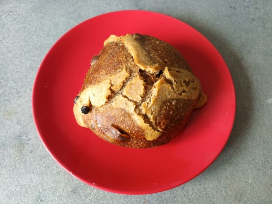 A large, yeast-risen hot cross bun sitting on a red plate.