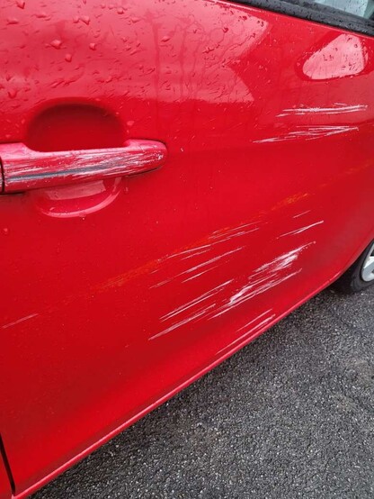 A red car, with deep scratches on the driver's door side.