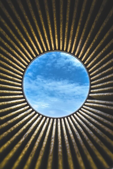A circular hole in a roof shows blue sky with a few clouds above