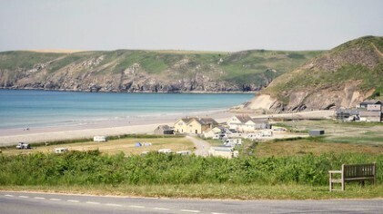 A sunny coastal bay with blue sea & sky, cliffs, small village. 