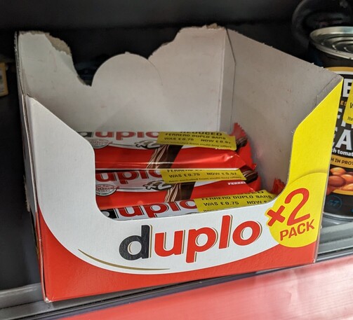 A box on a shop shelf containing chocolate bars. Both the box and bars are branded "Duplo"