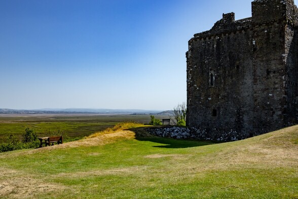 Weobly Castle overlooking the Lougher Estuary.

A Grey stone castle stands on the edge of high ground. Below a green salt marsh extends into the distance where a wide tidal river can be seen