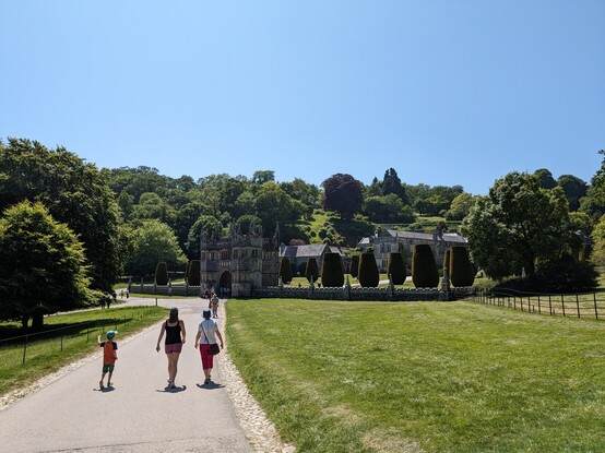 A path leads to a gatehouse with a large stately home and gardens within
