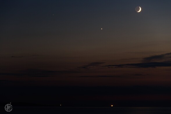 Mars, Venus and the crescent moon descent into the last of the orange twilight over Anglesey. Point Lynas lightbouse and the lights of a ship at anchor are visible on the horizon