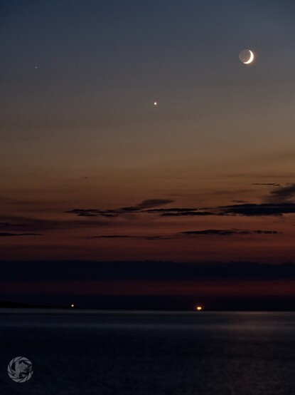 Mars, Venus and the crescent moon descent into the last of the orange twilight over Anglesey. Point Lynas lightbouse and the lights of a ship at anchor are visible on the horizon