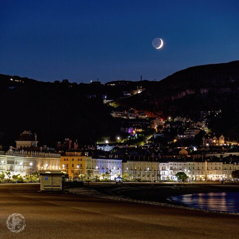 Venus and the crescent moon set behind the Great Orme. Taken from the promenade, the hotel buildings are all lit up. The lights on the houses highlight the route of Ty Gwyn road up the hillside