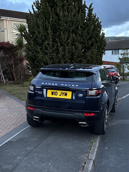 A black Range Rover parked entirely on the footpath so you have to either walk on the road or a garden to get past. 
