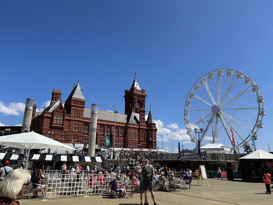 The red brick Pierhead building in Cardiff Bay with a big wheel and festival stands in the Road Dahl Plas. Bright blue skies. 
