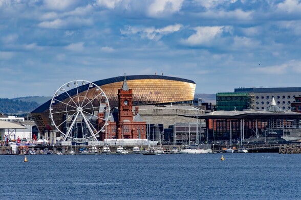 Looking to Cardiff Bay from the Barrage:

Calm blue water terminates in a line of moored boats. Behind them are the iconic buildings of the "new" cardiff bay. A white Ferris wheel, the Terracotta "Pierhead" building with it's clocktower and the glass-walled "Senedd" building. Rising behind all these is the impressive "Wales Millennium Centre" It's bronze coloured walls looking like fish scales