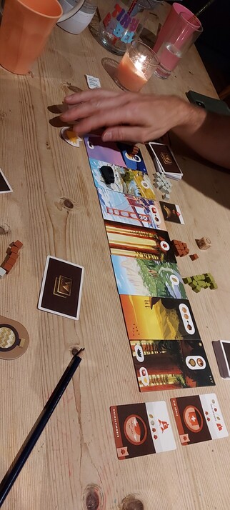 A bunch of scenic cards laying next to each other make the trail. There are cubes for resources and tiny meeples with hats and sticks.