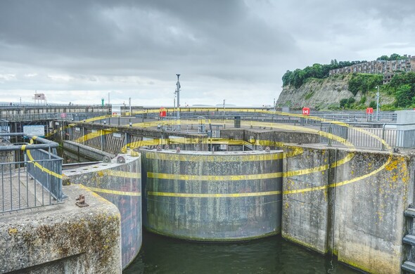 Looking across the sea lock as on Cardiff Bay Barrage from a specific spot where a series of yellow painted lines come together to look like a set of 3concentric rings spanning the surface of the lock walls, gates and railings 