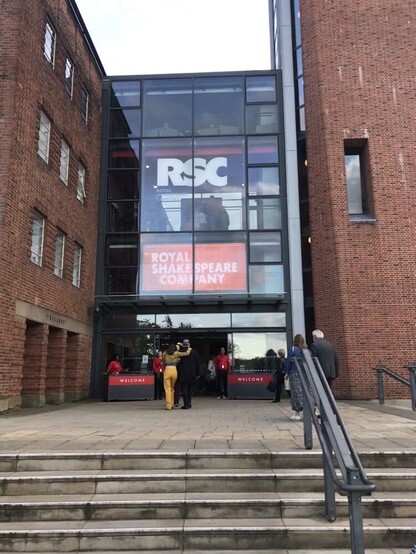 Stairs leading to the entrance of the Royal Shakespeare Company theatre. There is a large digital display that reads, "RSC" and "Royal Shakespeare Company", and stands reading "Welcome".
