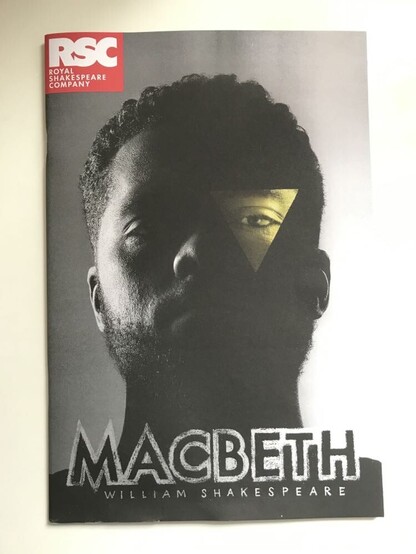 The cover of the programme for the RSC's production of Macbeth. It has a black and white headshot of Ruben Joseph, who has a yellow coloured tringle over his left eye.
At the top left there is a  red logo that reads, "RSC: Royal Shakespeare Company".
At the bottom the title reads, "Macbeth: William Shakespeare".