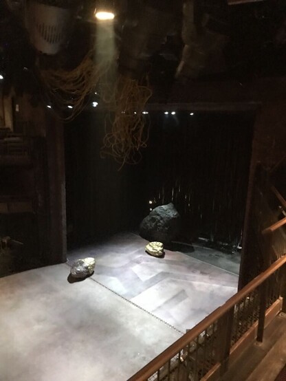 A theatre stage that extends out from the proscenium. It is empty except for three prop boulders.