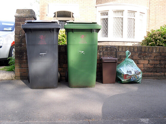 Selection of wheelie bins and a food caddie out for collection by a garden wall
